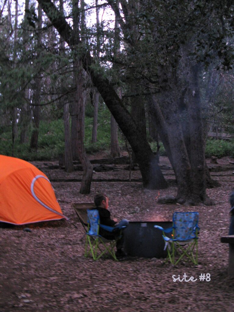 Orange Woods tent with young boy sitting next to campfire.
